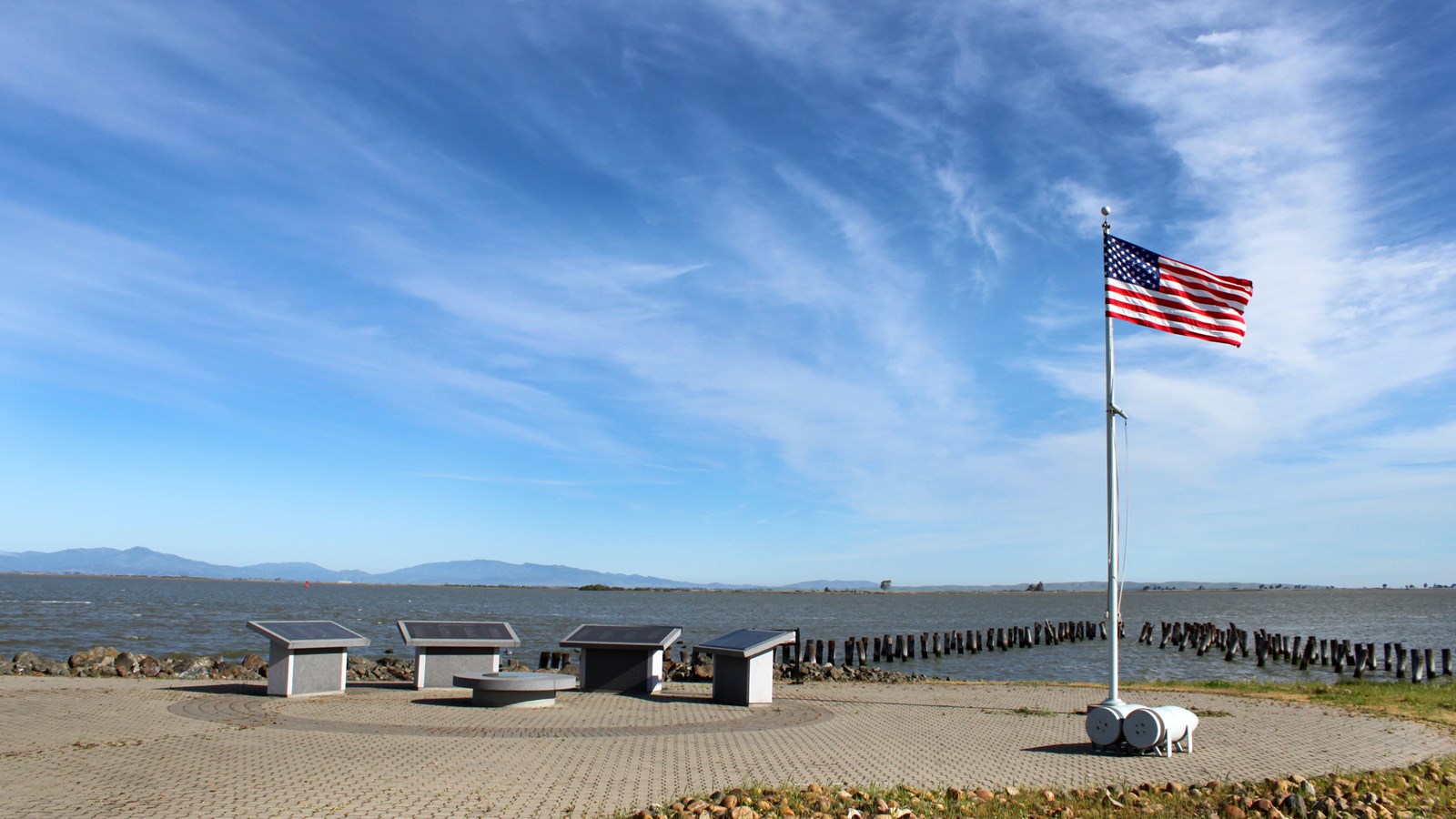 Interpretive panels and a flag at Port Chicago Naval Magazine National Memorial with Suisun Bay behind them.