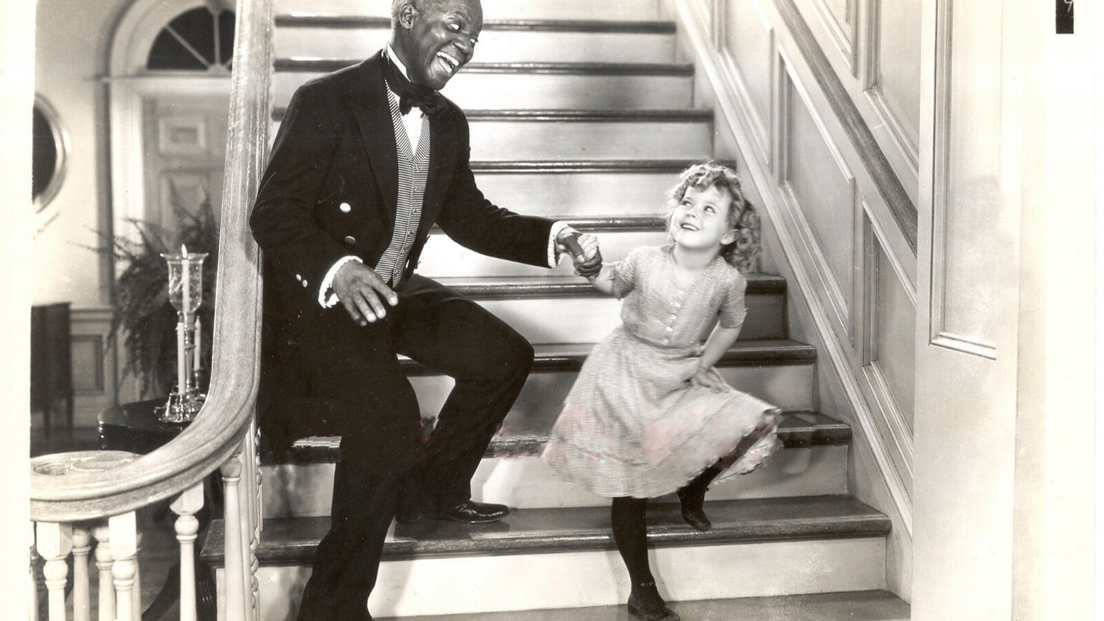 Black-and-white 1935 publicity still of Bill Robinson and Shirley Temple holding hands while dancing on a staircase in The Little Colonel.